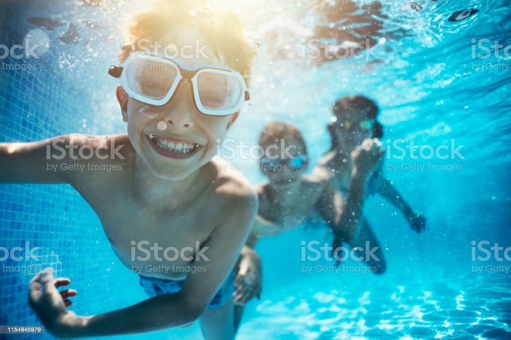 Happy kids having underwater party in the swimming pool. The boy is grinning at the camera. 
Shot with Nikon D850.