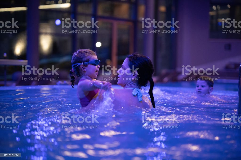 Young mother swimming in hotel pool with her playful little daughter